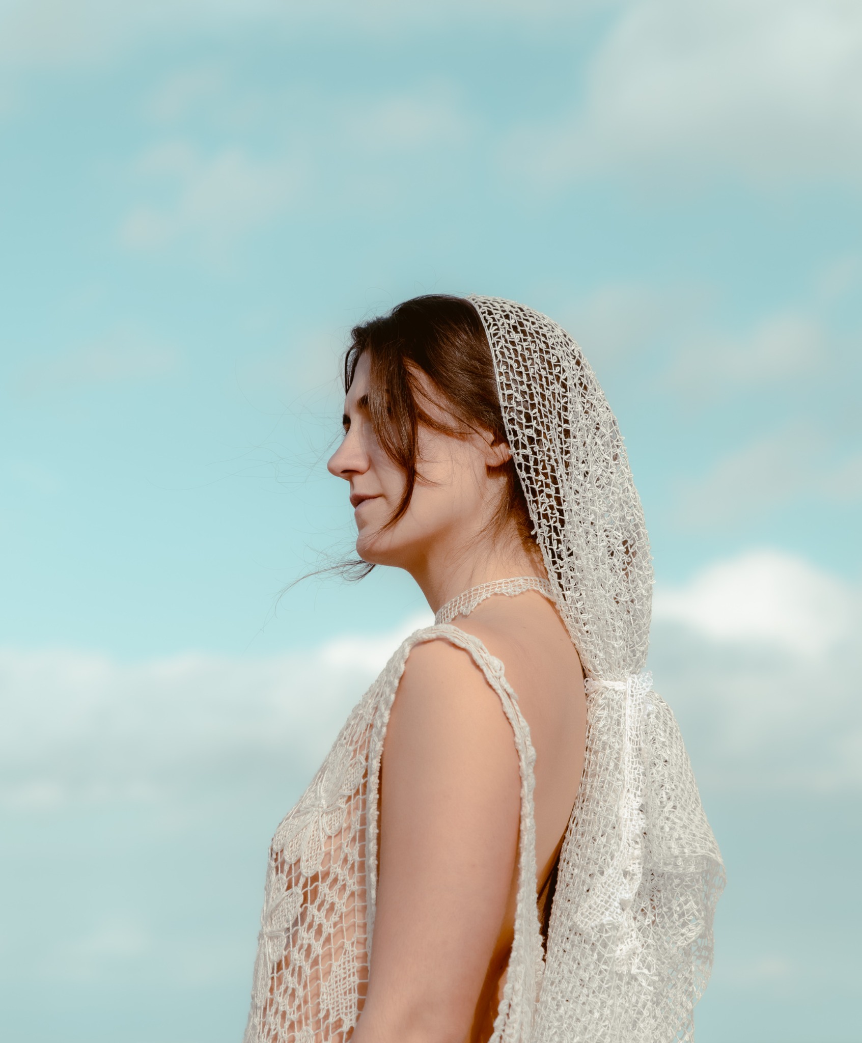 Retrato de perfil con tejido de ñandutí frente al cielo